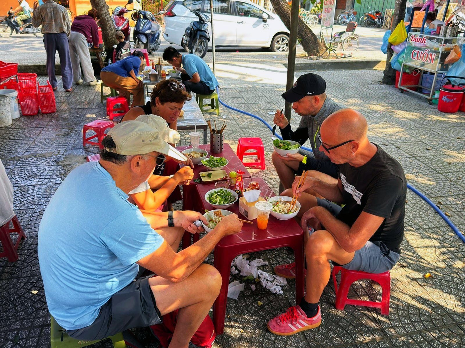 Travellers sharing a street-food breakfast at a roadside table in Hoi An, Vietnam