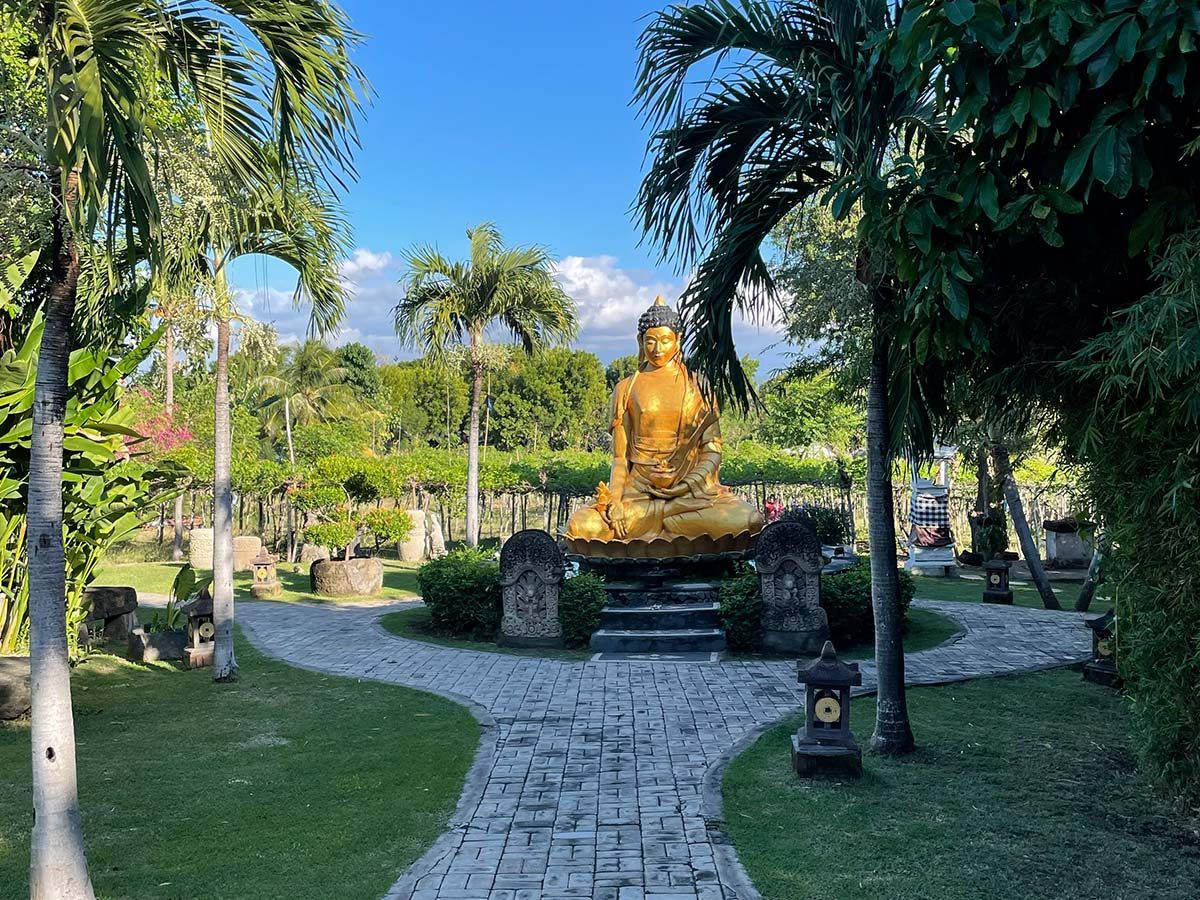 A golden Buddha statue on a lotus pedestal in a tropical garden with palms and a curved stone path