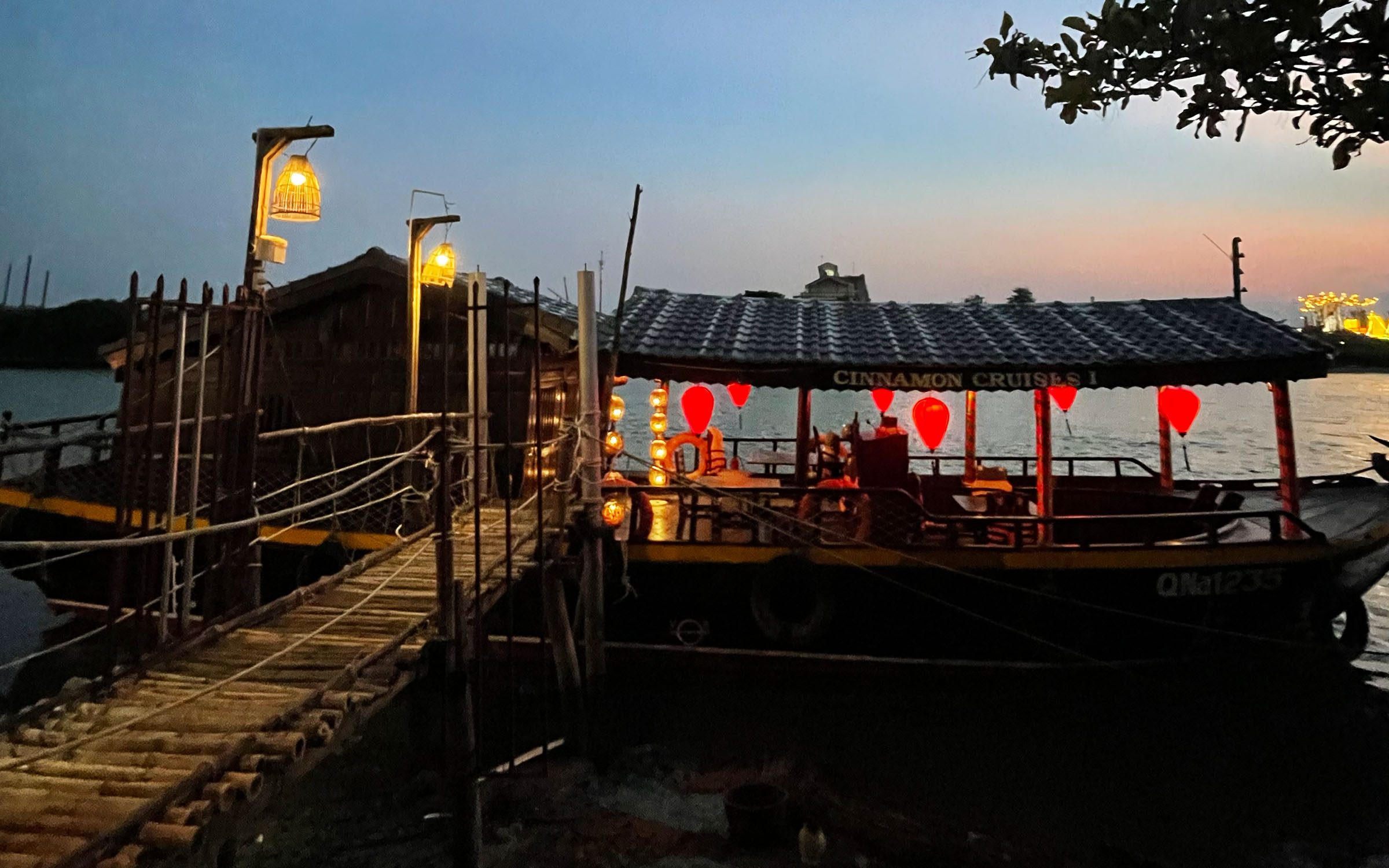Ł&oacute;dź oświetlona lampionami przycumowana do drewnianego pomostu na rzece w Hoi An o zmierzchu